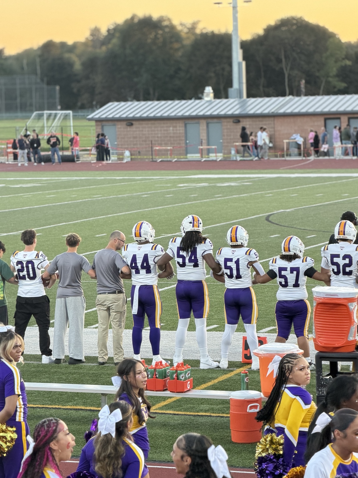 Troy High School players standing arm in arm on the sideline, Joseph Fleuriot III in number 54 at center