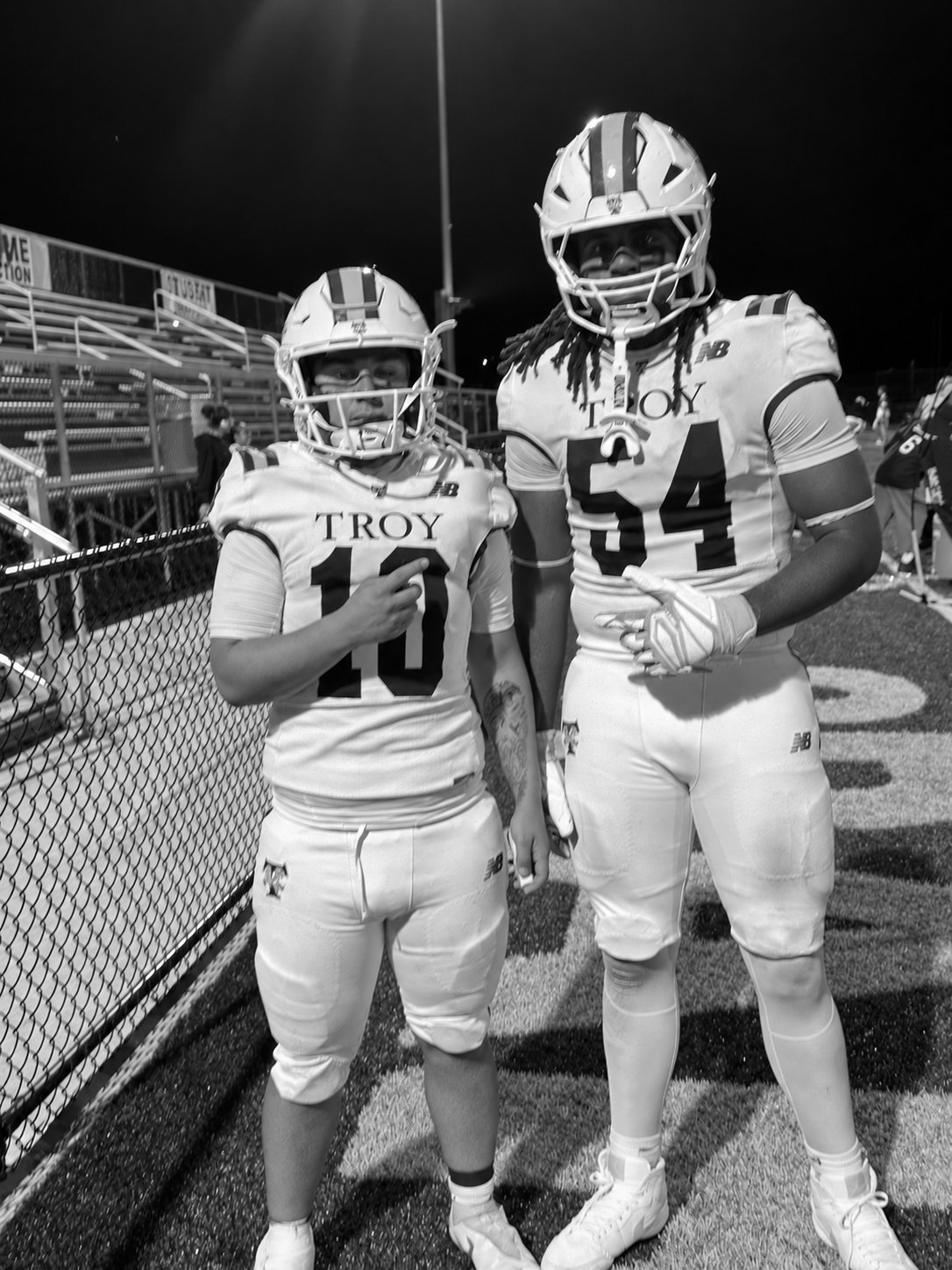 Black-and-white photo of Joseph Fleuriot III in number 54 standing beside his Troy teammate in number 10 under the stadium lights